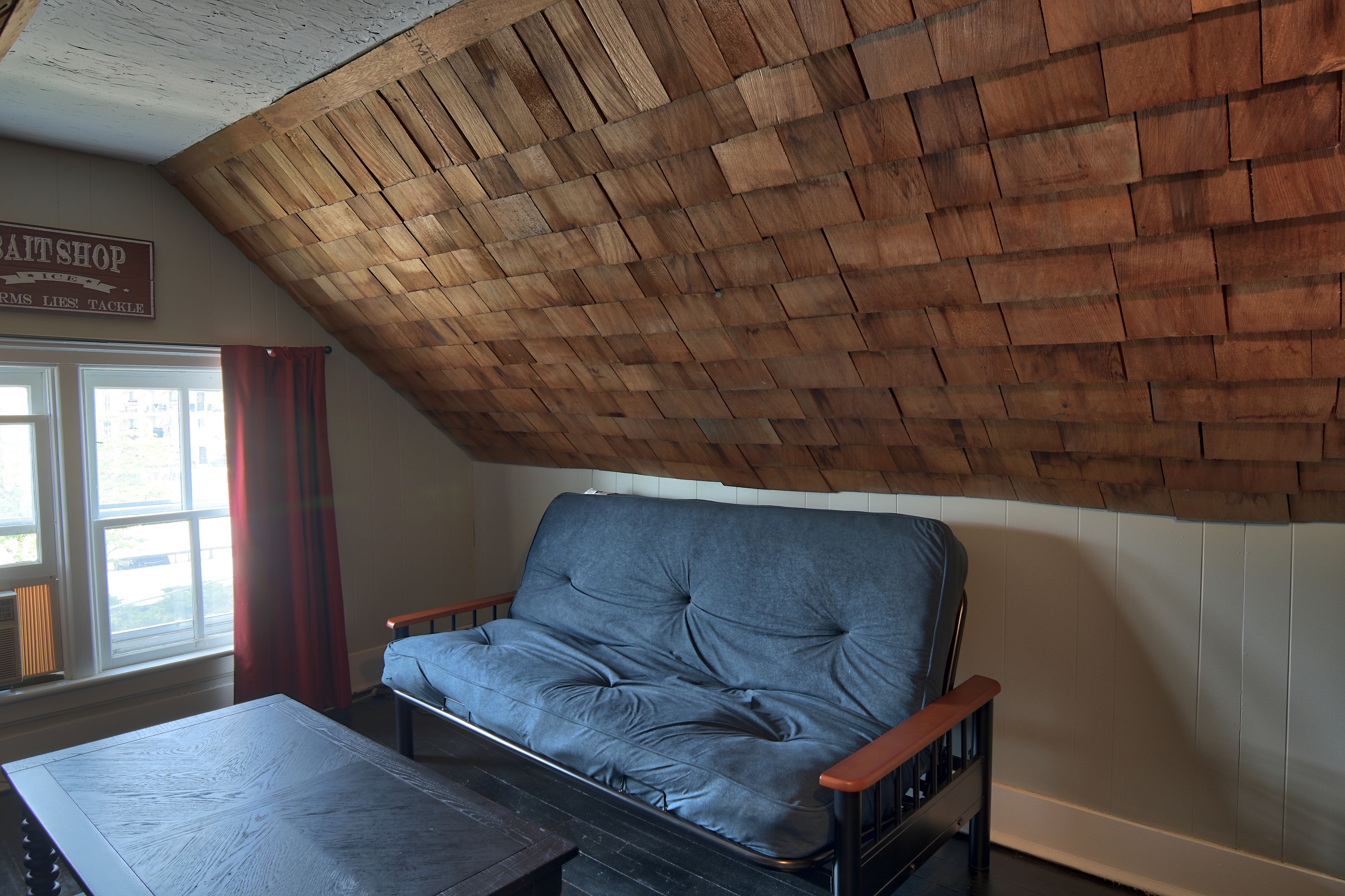 A room with a wooden ceiling, a blue sofa, a wooden table, and a window with a view.