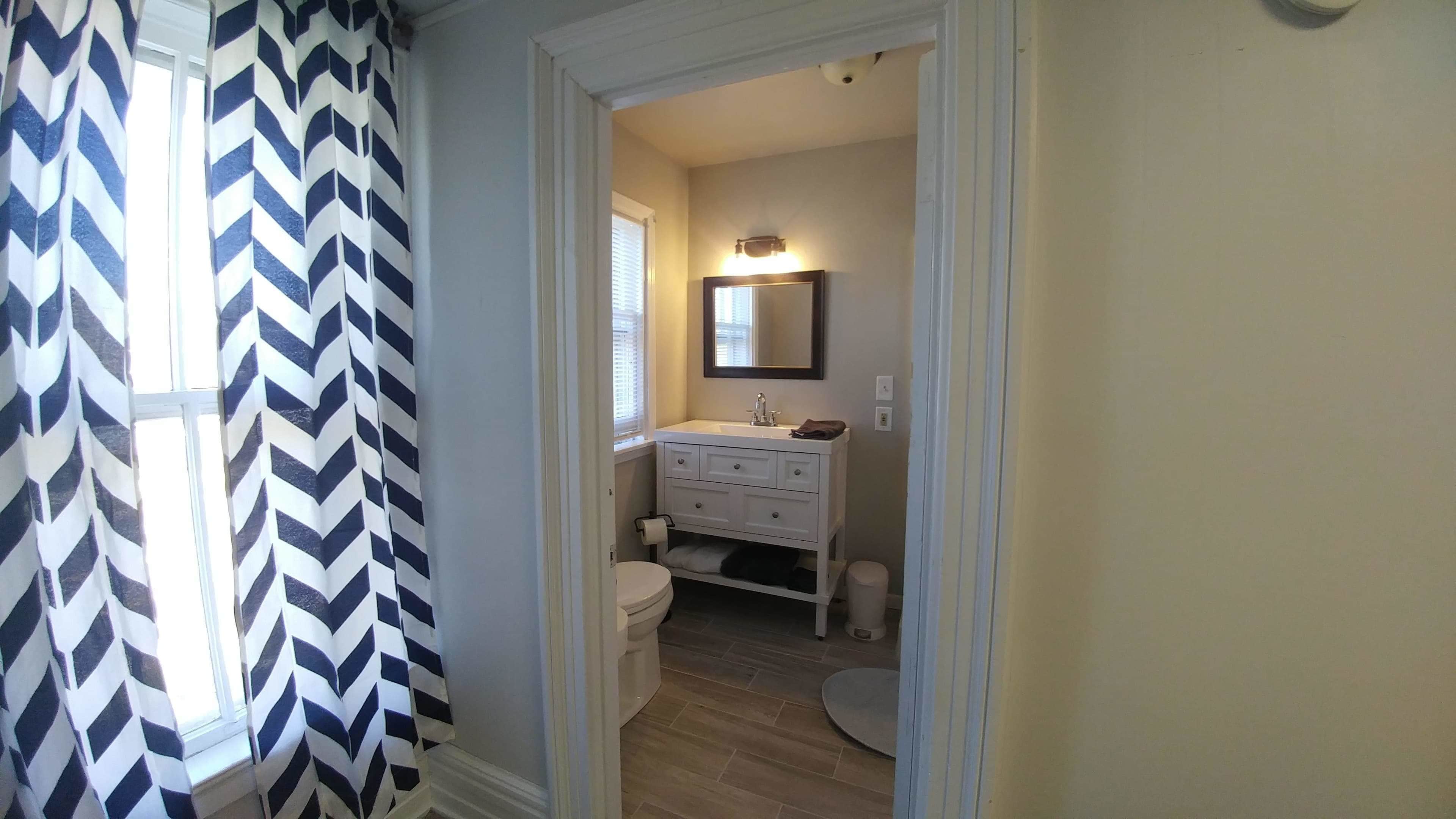 A narrow hallway leading to a bathroom with a white vanity, a mirror, and a toilet.