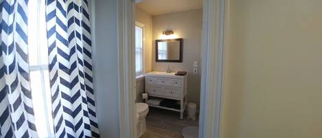 A narrow hallway leading to a bathroom with a white vanity, a mirror, and a toilet.