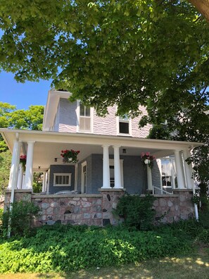 A two-story house with a stone foundation, a covered porch with white columns, and a stone exterior. - Charlevoix House (Charlevoix)