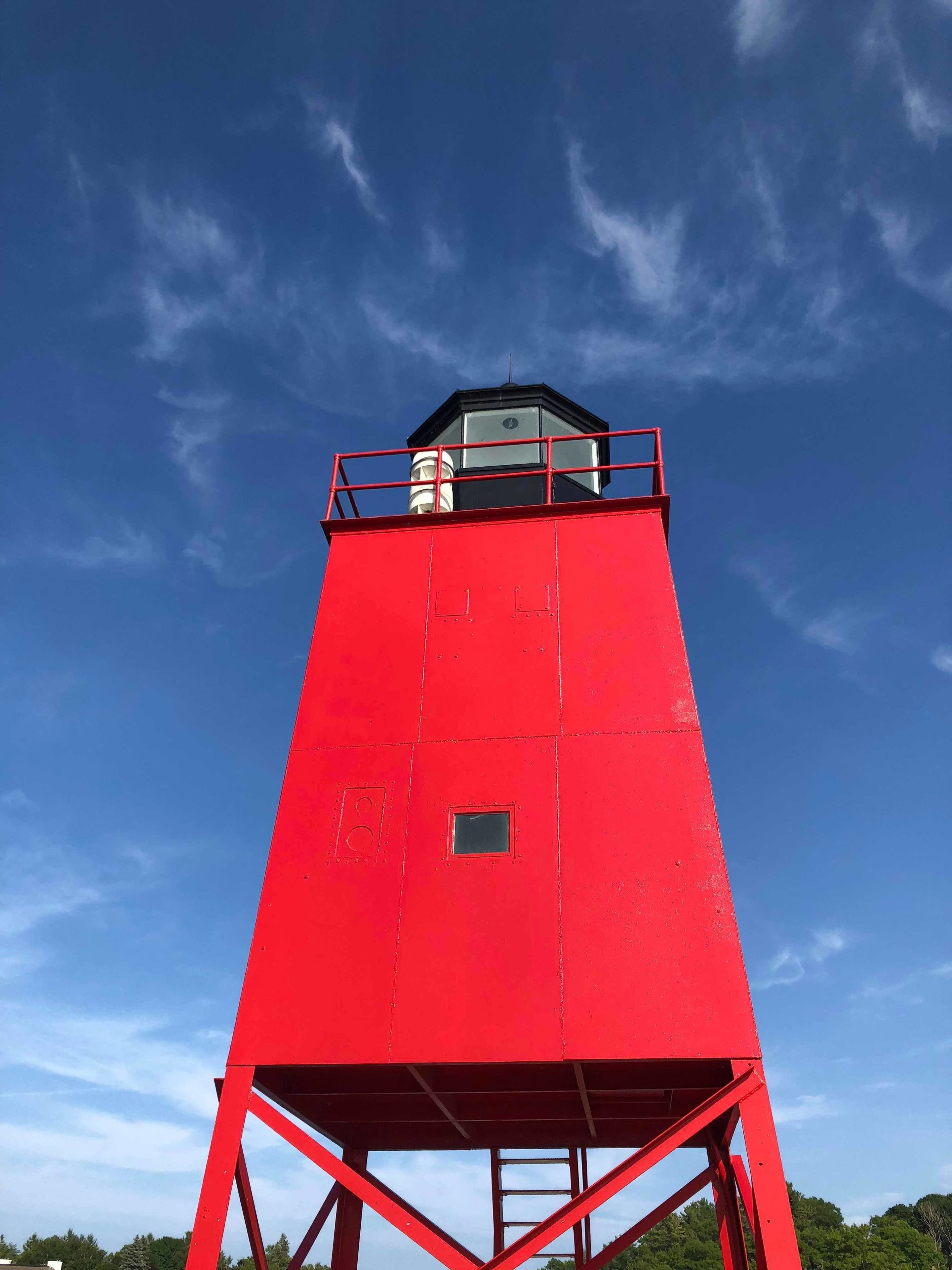 Un phare rouge avec une petite plateforme d’observation et un ciel dégagé en arrière-plan.