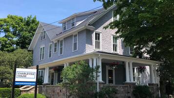 A two-story house with a stone foundation, a covered porch, and a sign indicating it is for sale.