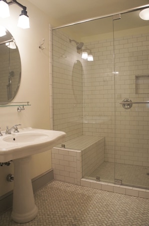 Bathroom features a pedestal sink, glass-enclosed shower, and a round mirror.