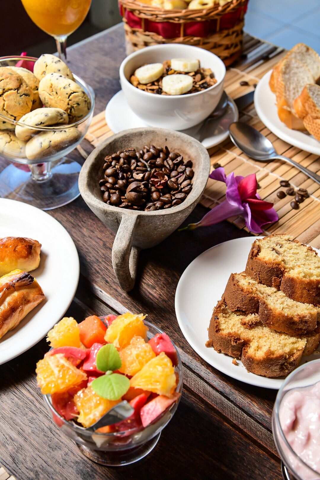 A breakfast table with various food items including cookies, coffee beans, fruit, and bread.