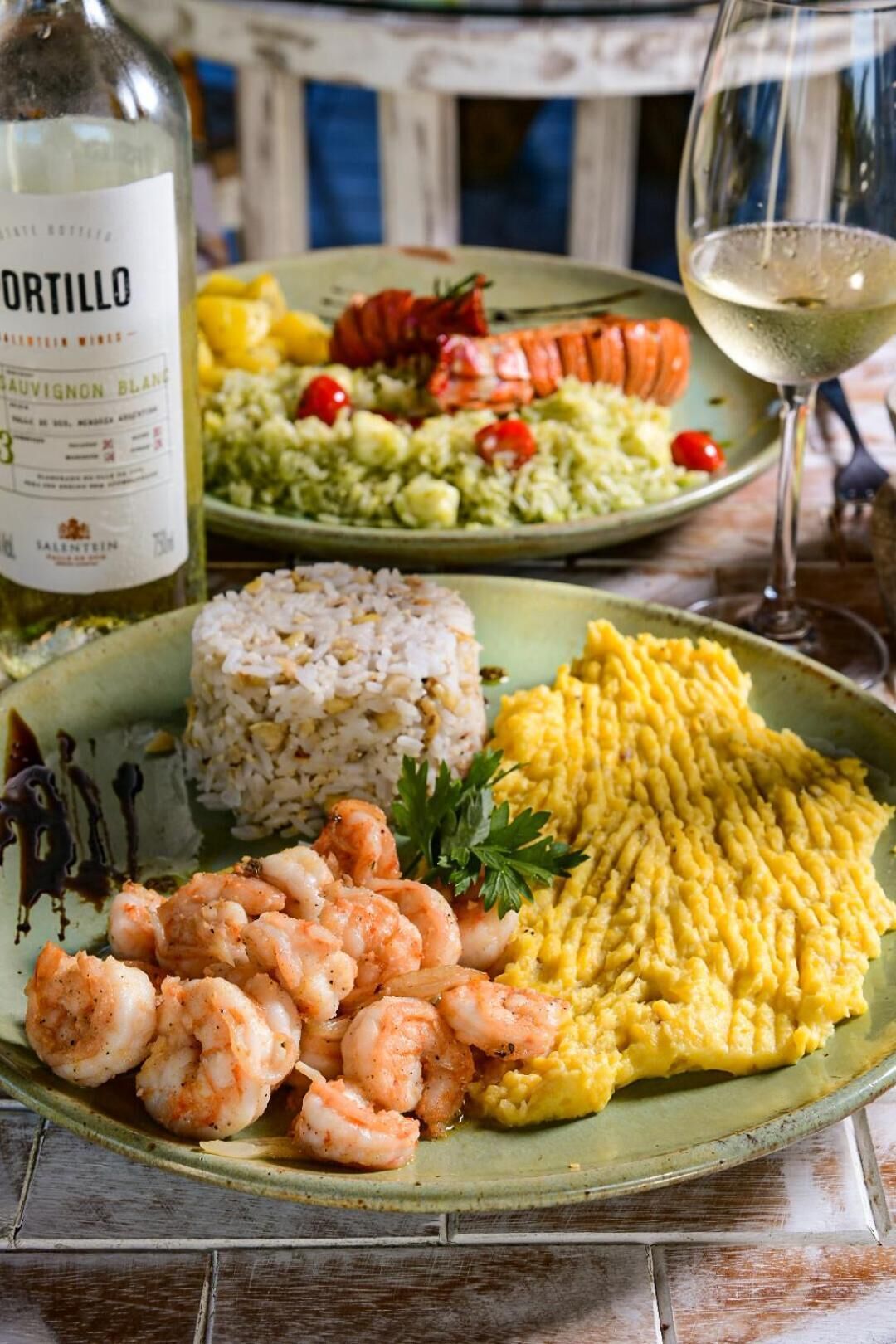 A plate with rice, shrimp, and yellow food, a bottle of wine, and a glass of white wine on a table.