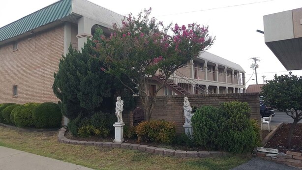 A building with a brick facade, a covered walkway, and two statues in the front garden. - Cactus Inn and Suites (Copperas Cove)