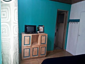 Ein Zimmer mit Türkiswänden, einer Holzkommode mit Fernseher darauf und einer Tür zu einem weiteren Raum.