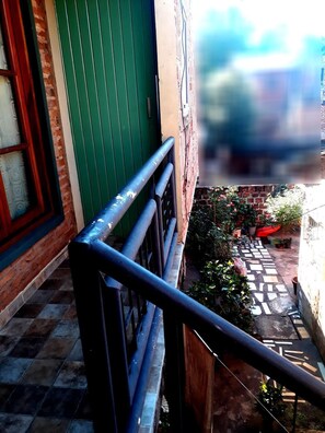 A narrow outdoor corridor with a metal railing, a green door, and a tiled pathway leading to a brick wall with potted plants. - El Rinconcito (Puerto Iguazú)