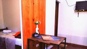 A small room with a wooden table, a bench, a bed, and a TV mounted on the wall. - El Rinconcito (Puerto Iguazú)