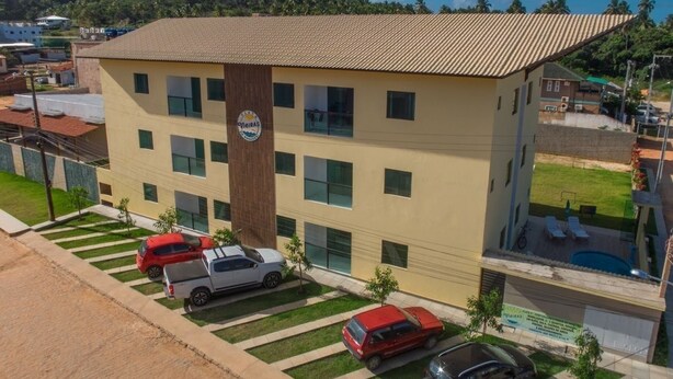 A multi-story building with a tiled roof, a central vertical sign, and a parking area with several cars. - Flats Vieiras do Maragogi (Maragogi)