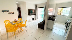 A modern apartment with a dining area featuring yellow chairs and a small table, a kitchenette with a stove and microwave, and a TV mounted on the wall. - Flats Vieiras do Maragogi (Maragogi)