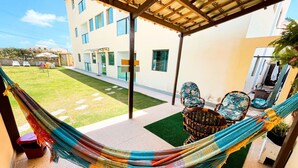 A hammock on a patio with a view of a building and a grassy area. - Flats Vieiras do Maragogi (Maragogi)