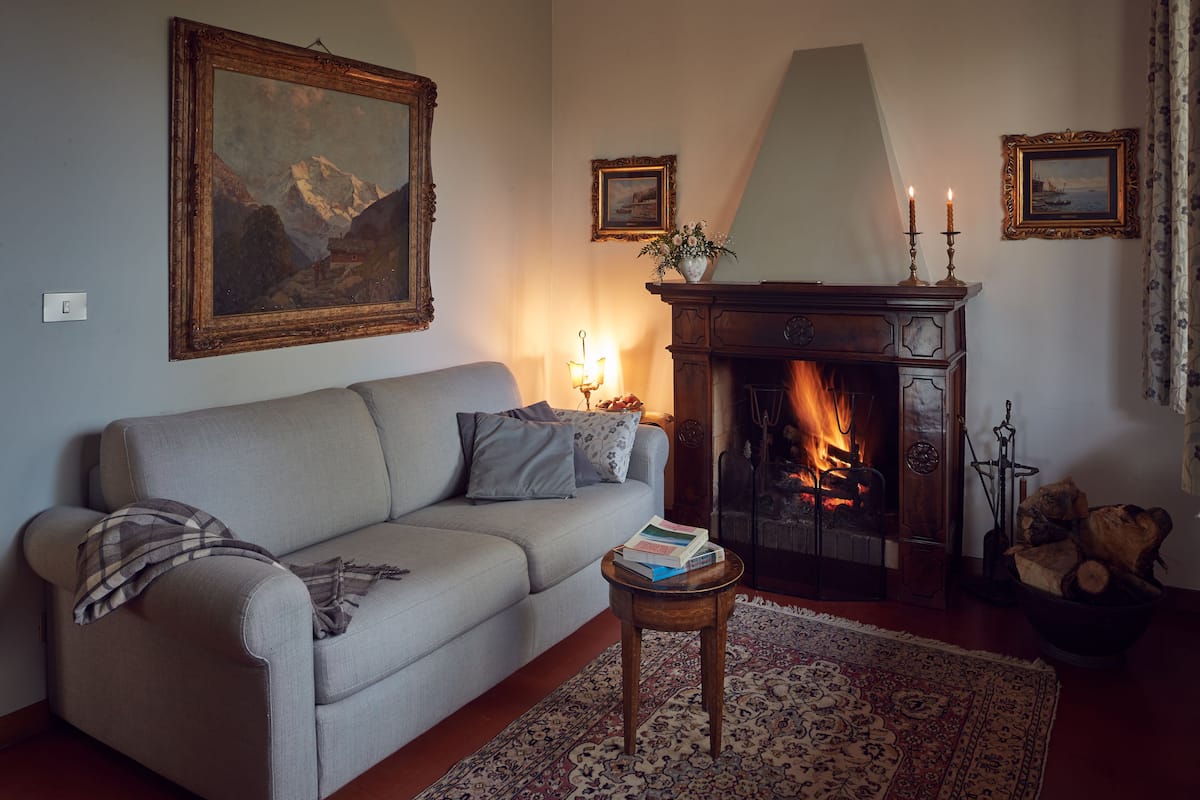 A living room with a sofa, a fireplace, a rug, and a painting on the wall.