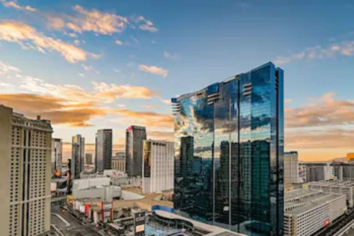 A modern cityscape with high-rise buildings, including a prominent glass skyscraper reflecting the sky.
