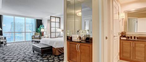 Habitación de hotel con una cama grande, una zona de estar con una silla y mesa, un armario de madera y un espejo grande.
