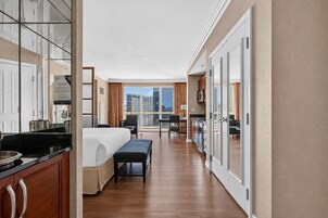 Quarto de hotel com cama, escrivaninha, cadeira, banco, cozinha compacta e varanda com vista.