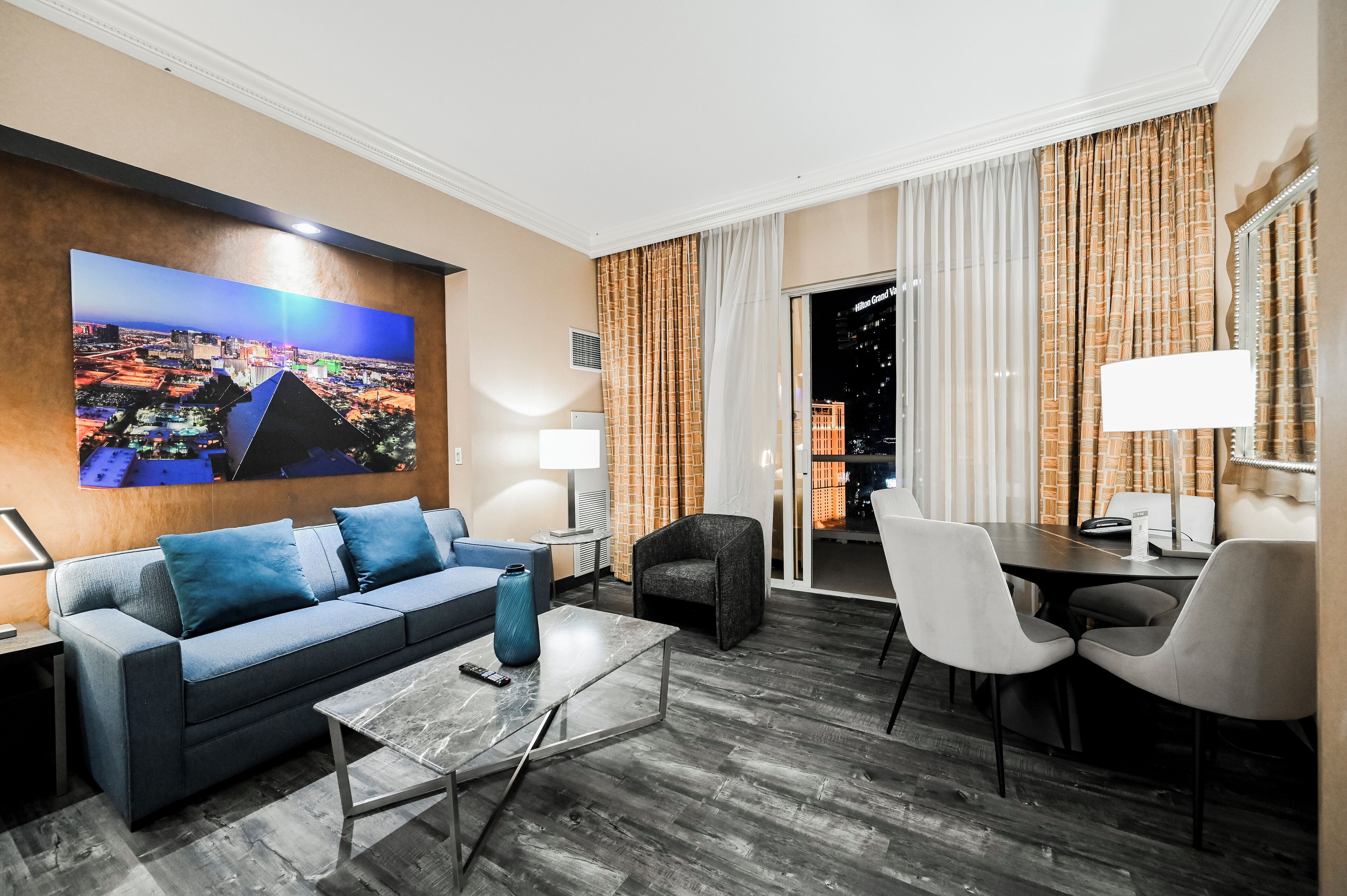A modern hotel room with a sofa, coffee table, and dining area.