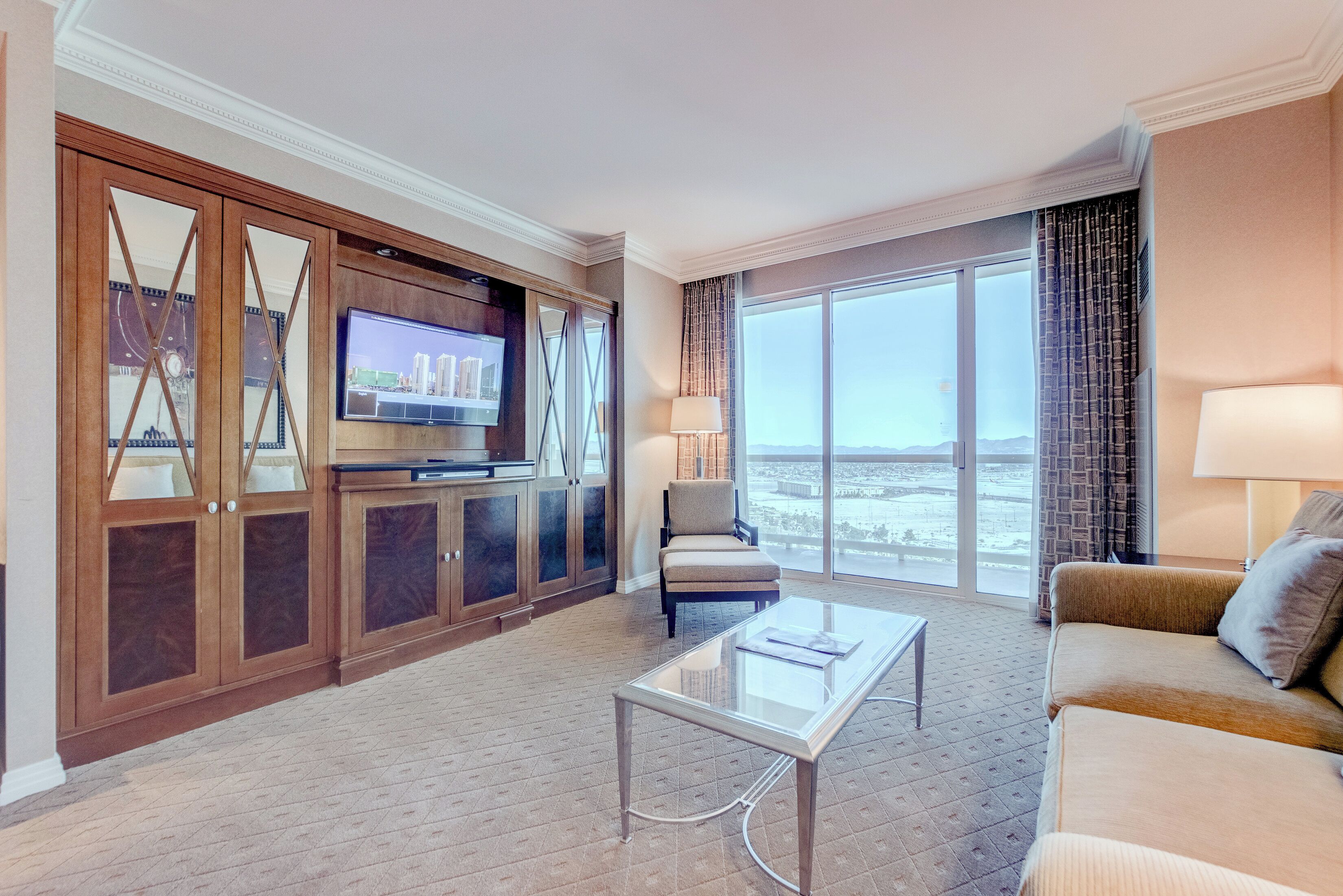 Ein Hotelzimmer mit großem Fenster, Flachbildfernseher, Sofa, Sessel und Couchtisch.