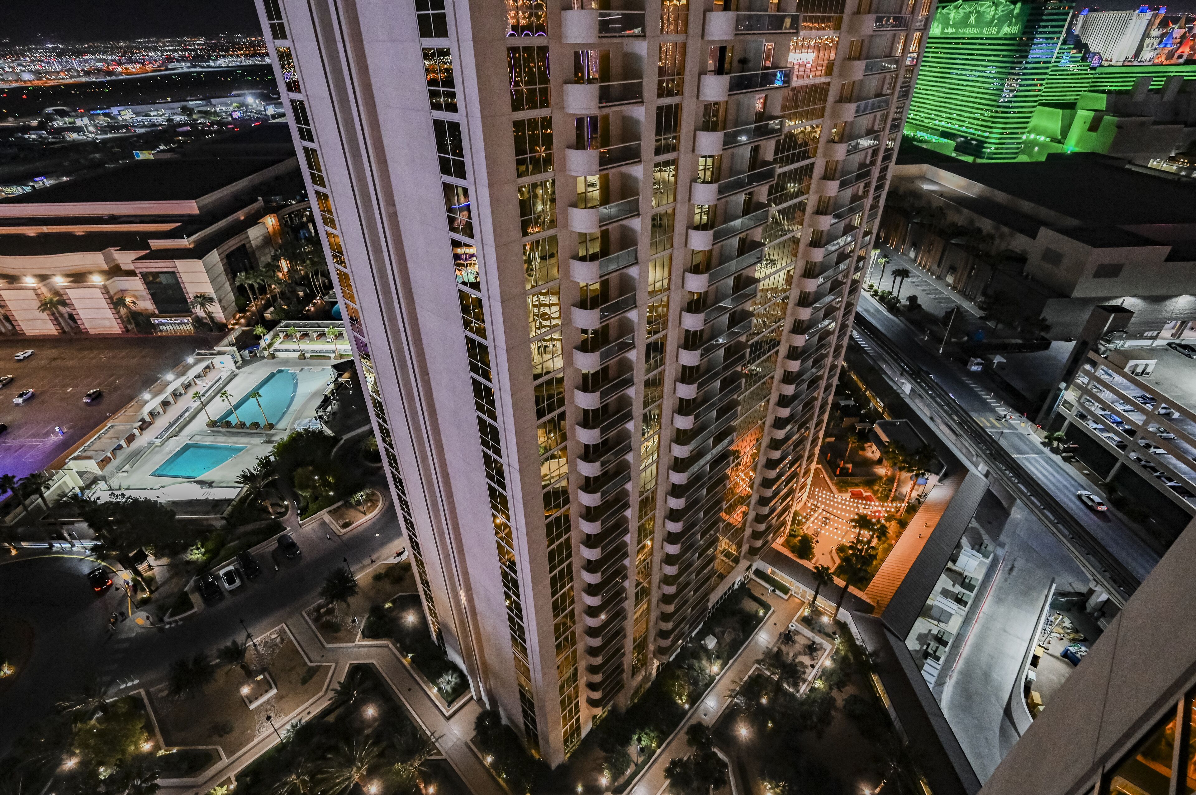 A high-rise building with multiple floors, a swimming pool, and a parking area.
