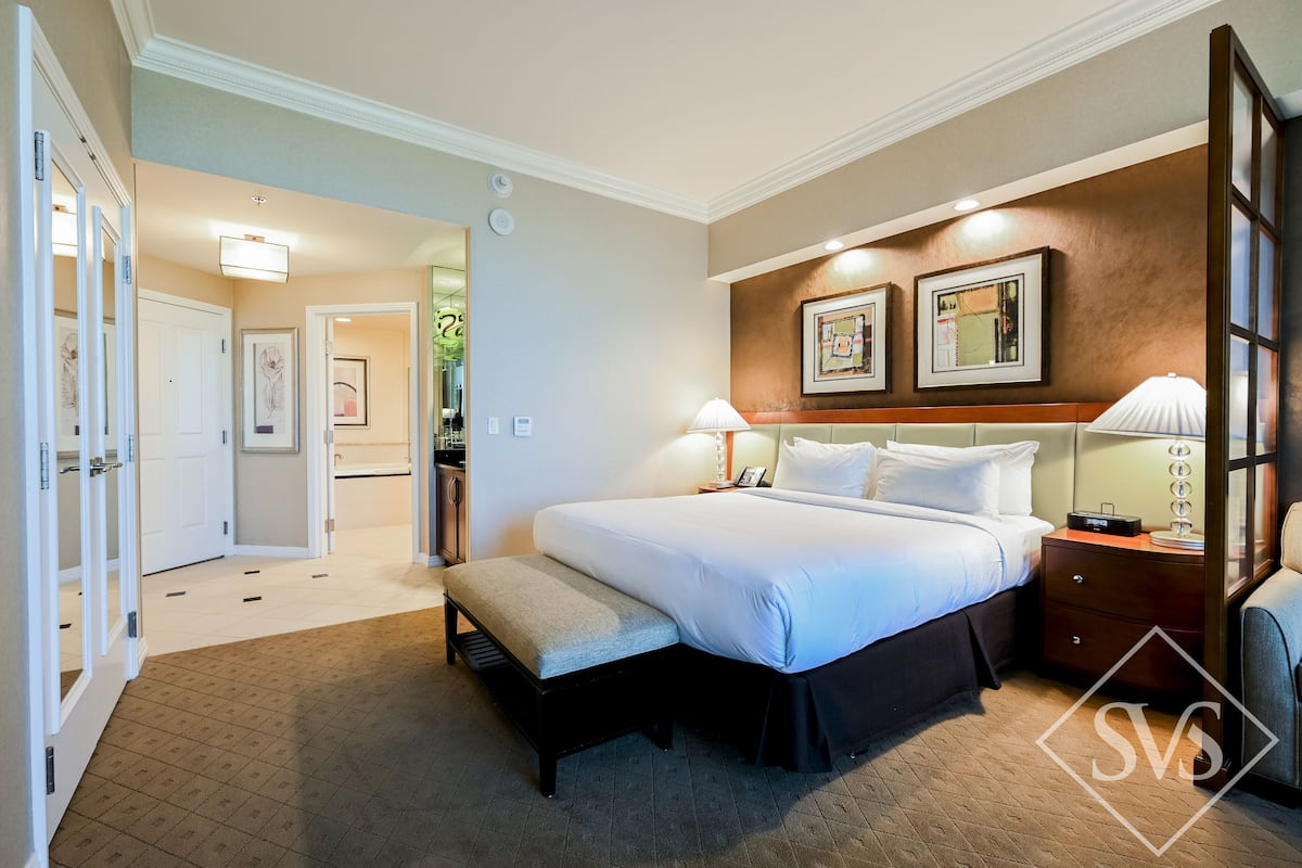 A hotel room with a large bed, bedside tables, a bench, and a mirror.