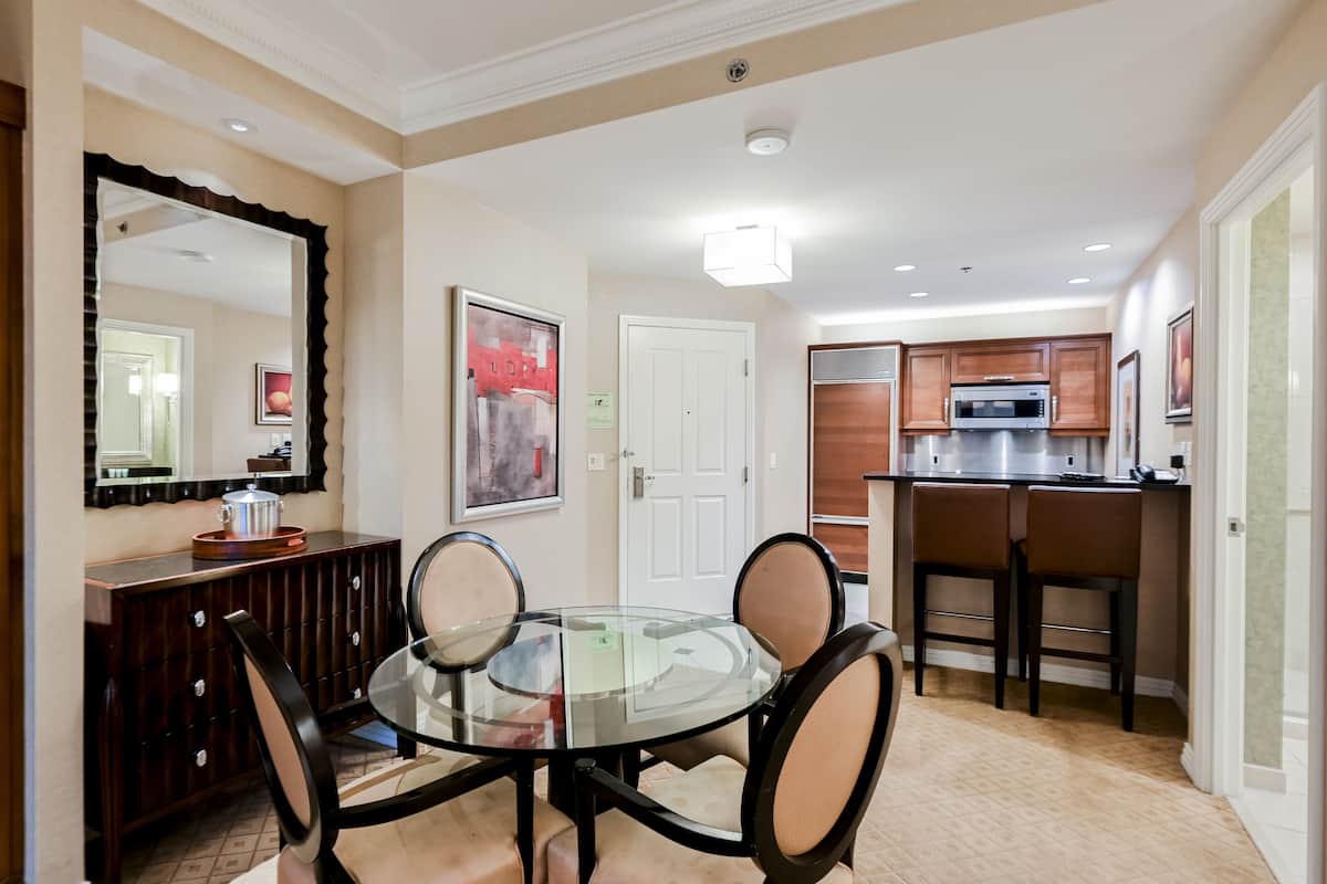 A dining area with a glass table, four chairs, a wooden cabinet, and a microwave in the background.