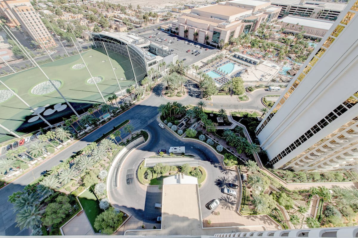 An aerial view of a hotel with a curved road, palm trees, and a swimming pool.