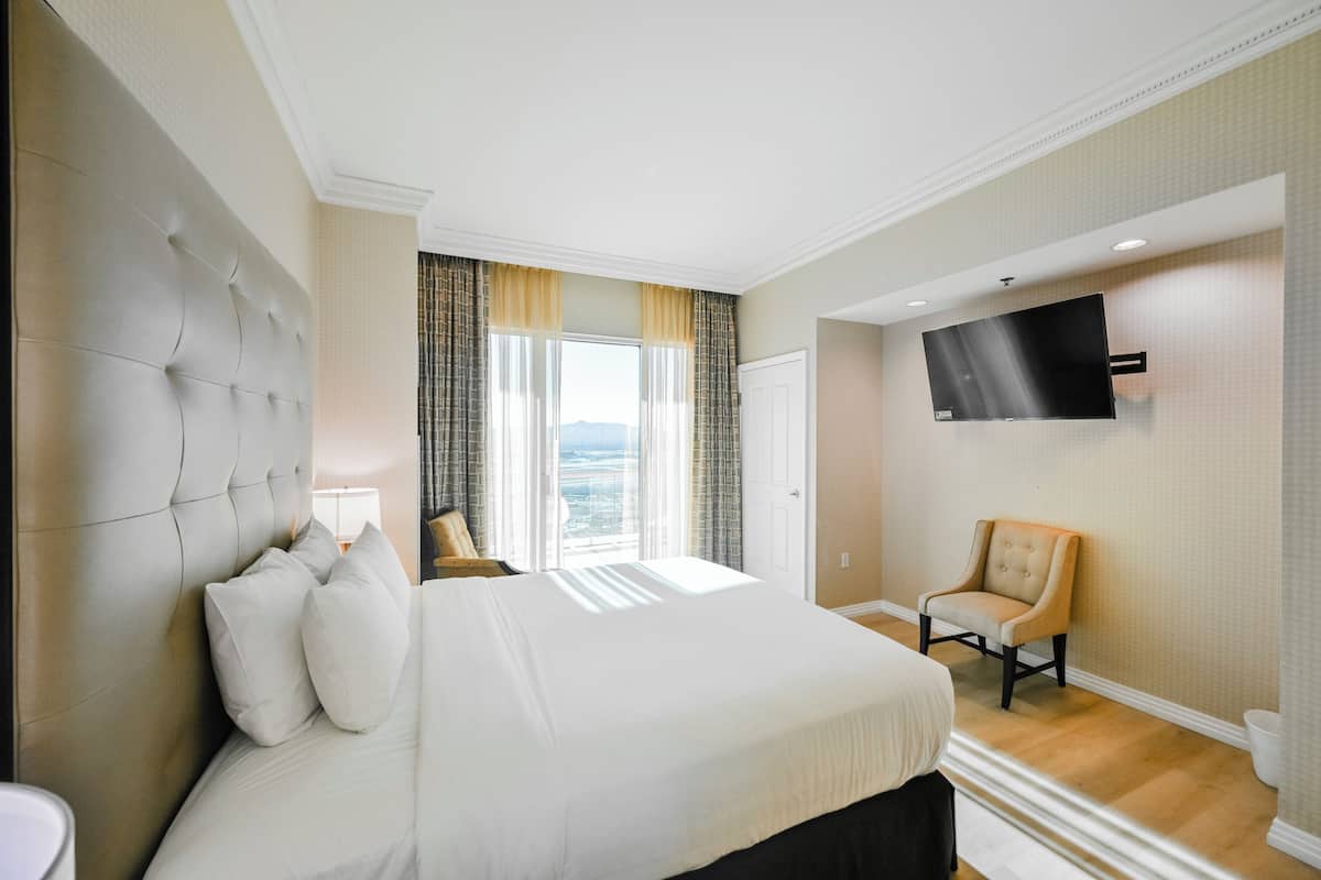 A hotel room with a large bed, a television mounted on the wall, and a view of the outdoors through the window.