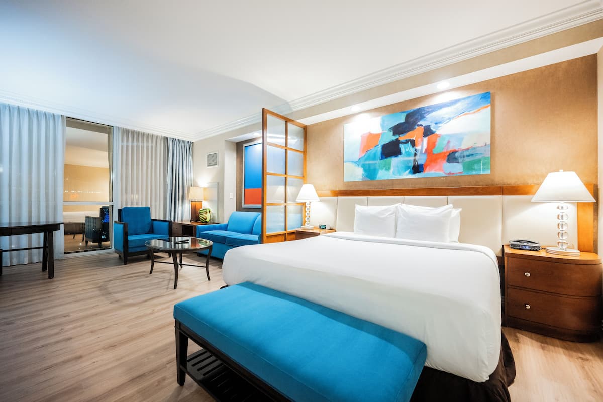 A hotel room with a large bed, a blue sofa, a small table, and a nightstand with lamps.