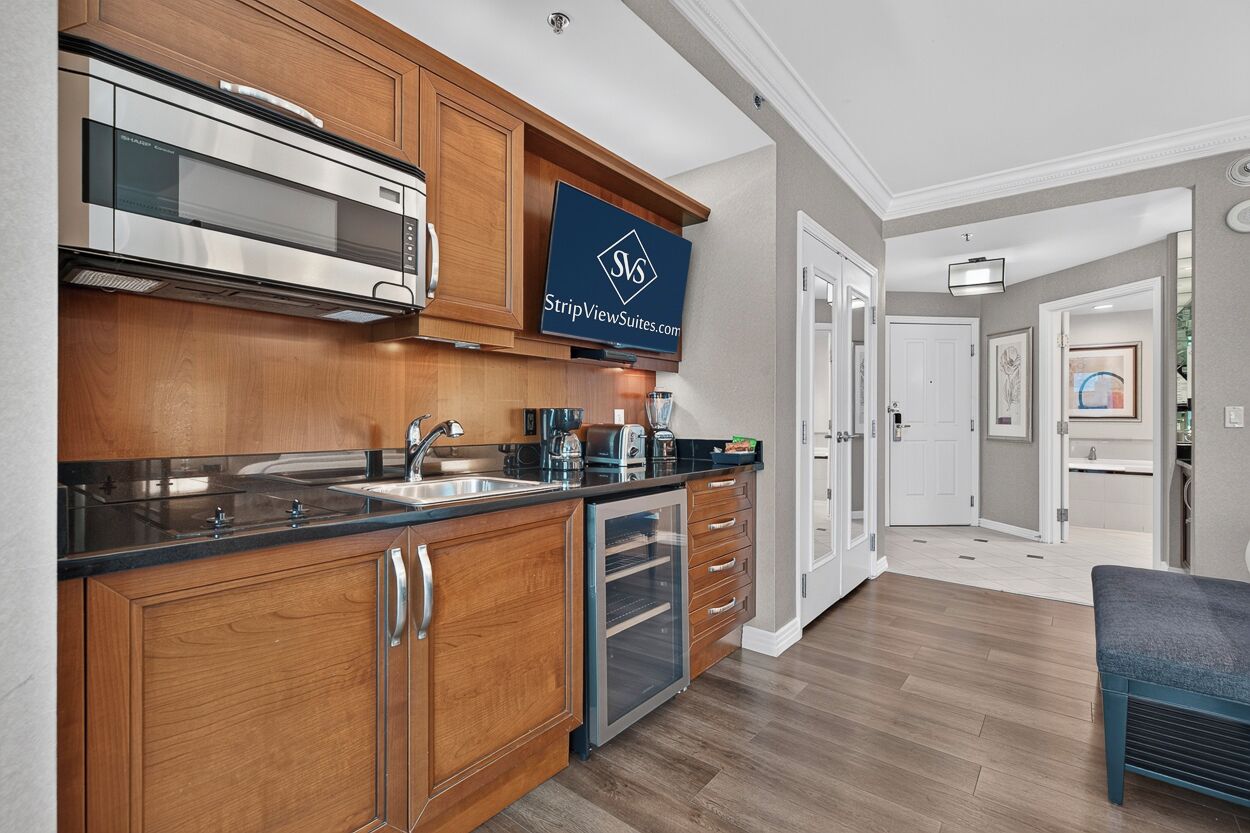 A modern kitchen with wooden cabinets, stainless steel appliances, and a visible logo on the wall.
