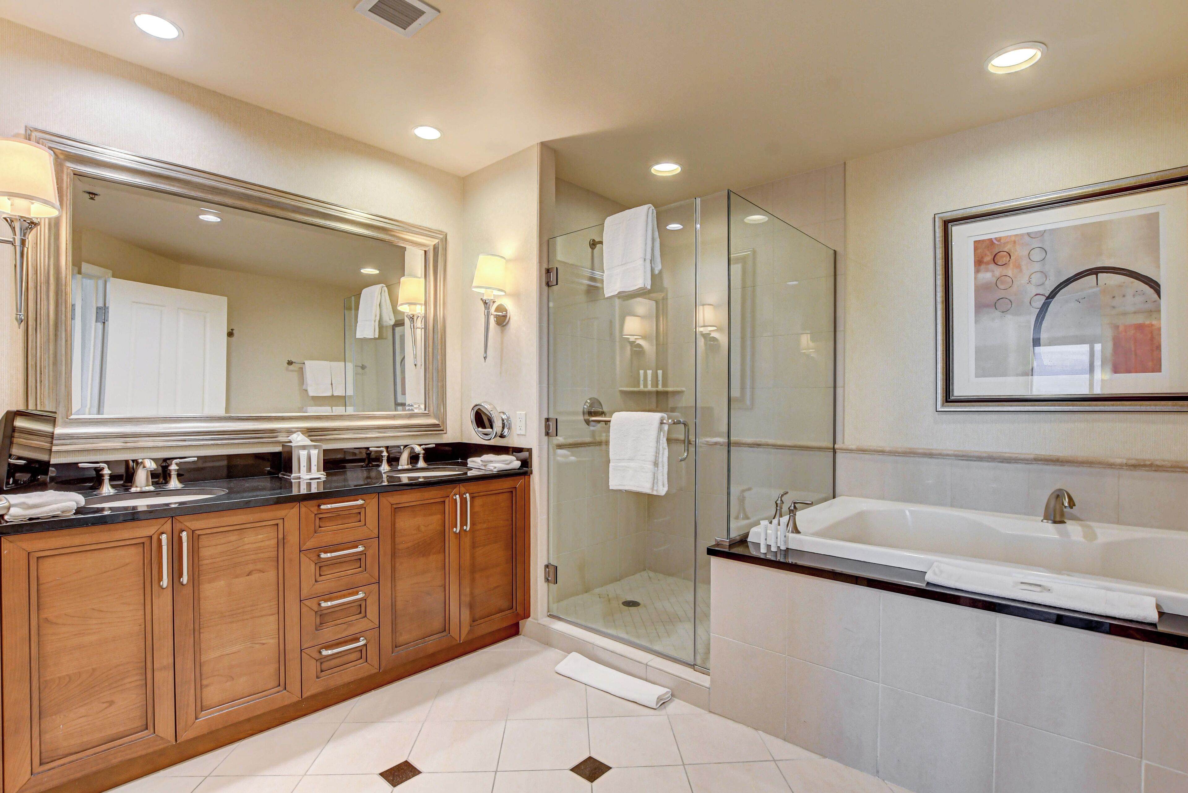 Un baño moderno con un espejo grande, ducha con cerramiento de vidrio, bañera y muebles de madera.