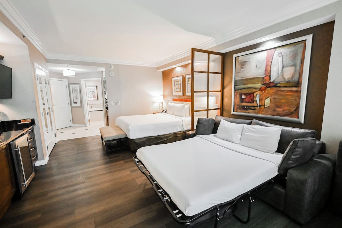 A hotel room with two beds, a sofa bed, a TV, and artwork on the wall.