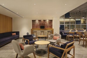 Relax in comfort with sofas, armchairs, and round tables, surrounded by a large abstract artwork and natural light.