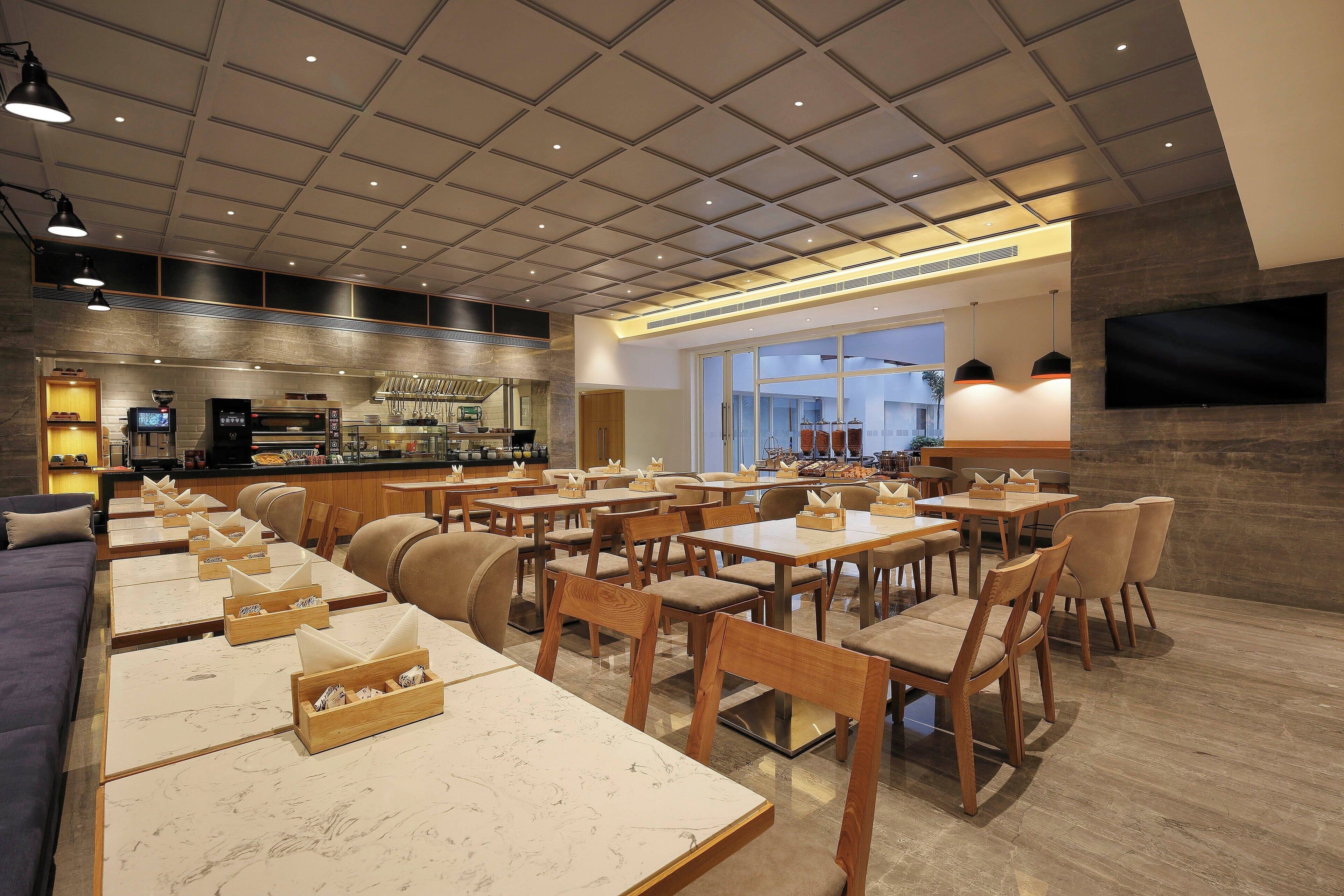 A restaurant with multiple dining tables and chairs, a kitchen area, and a large window providing a view.