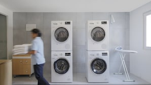 A modern laundry room with two stacked front-loading washing machines, a wooden cabinet, and a small ironing station. - Holiday Inn Express Bengaluru Yeshwantpur by IHG (Bengaluru)
