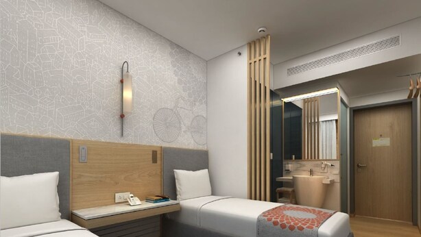 Ein Hotelzimmer mit zwei Einzelbetten, einem hölzernen Kopfteil, einem kleinen Schreibtisch mit Telefon, einem Spiegel und einem Badezimmer mit Waschbecken und Toilette.