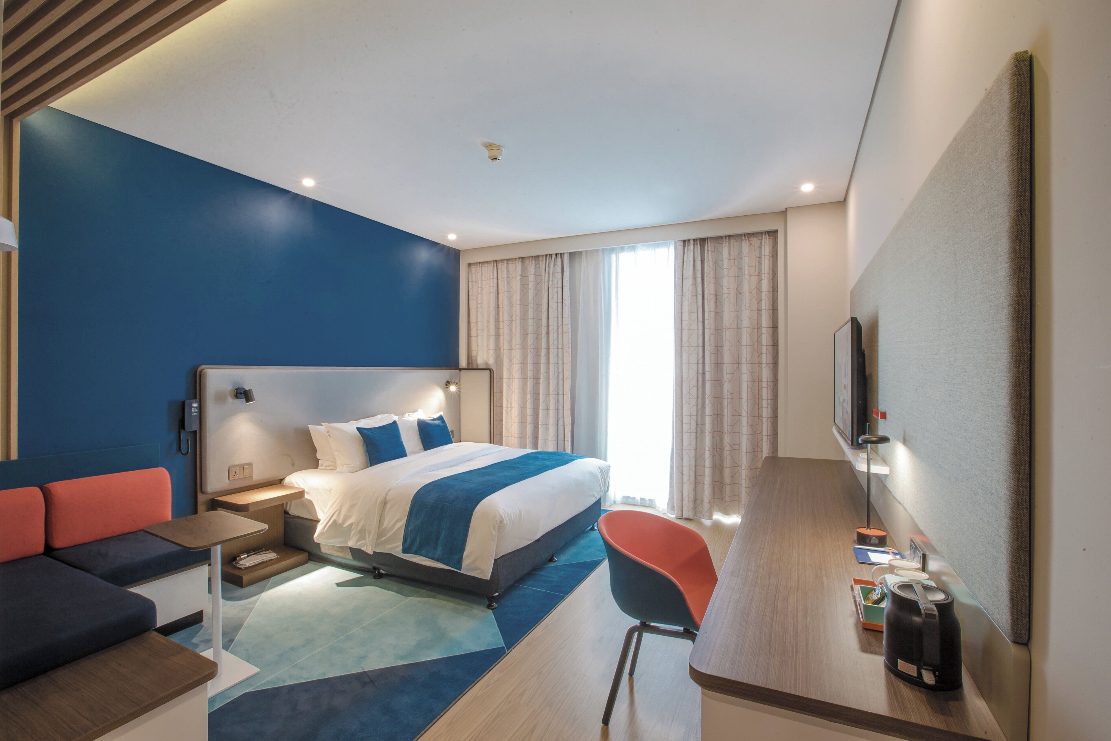 Una habitación de hotel moderna con una cama grande, un escritorio, una silla y un televisor.