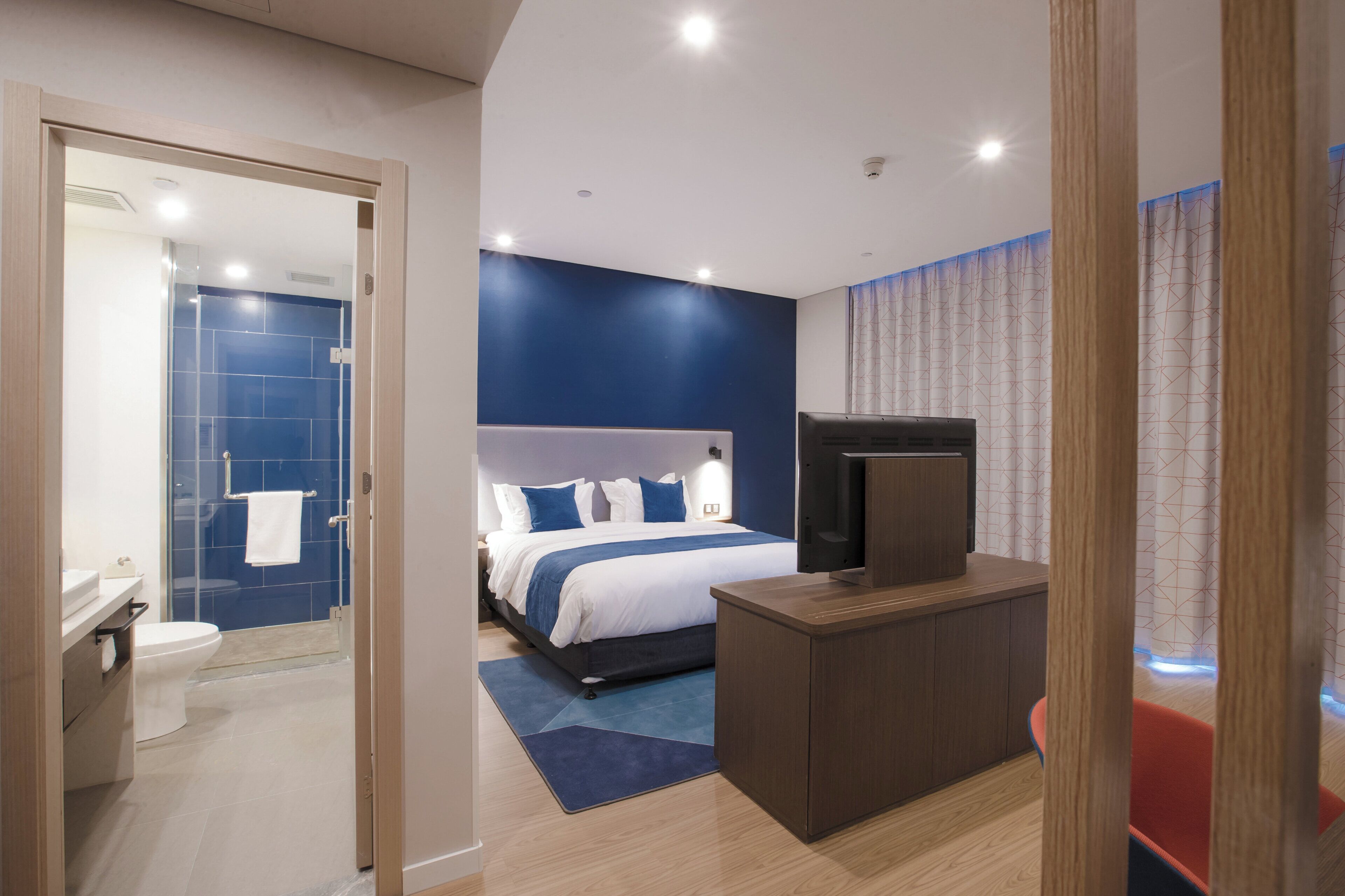 A hotel room with a bed, a TV, a desk, and a bathroom.