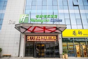 A Holiday Inn Express hotel with a modern glass facade, a prominent green and blue sign, and a digital display with Chinese characters. - Holiday Inn Express Hefei High Tech by IHG (Hefei)