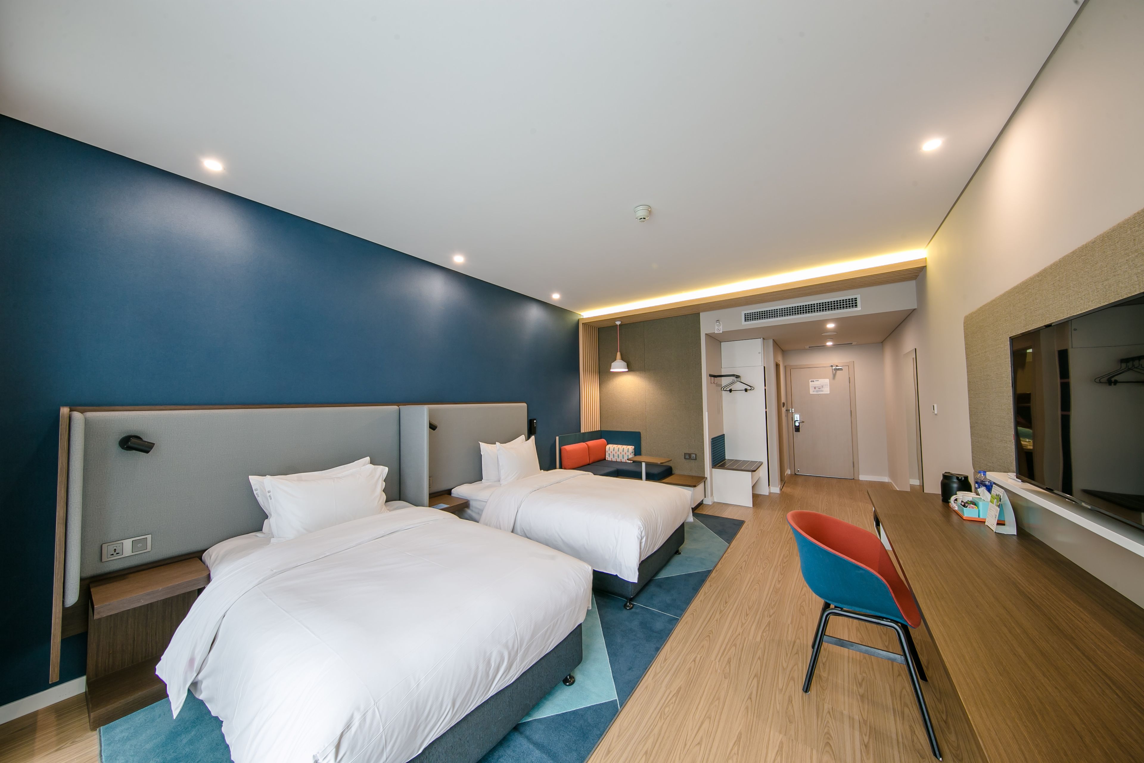 A modern hotel room with two beds, a dining area, and a TV.