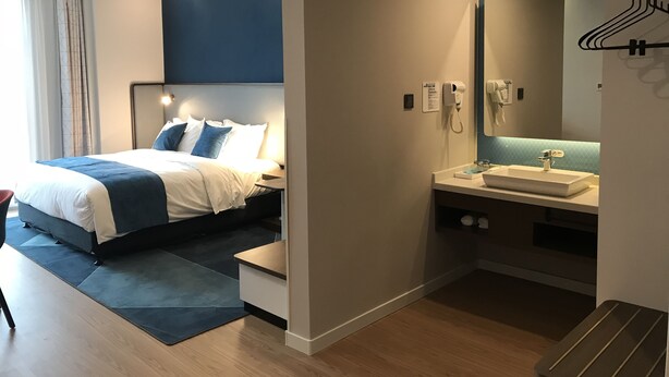 A modern hotel room with a bed, bedside table, and a bathroom with a sink and mirror. - Holiday Inn Express Hefei High Tech by IHG (Hefei)