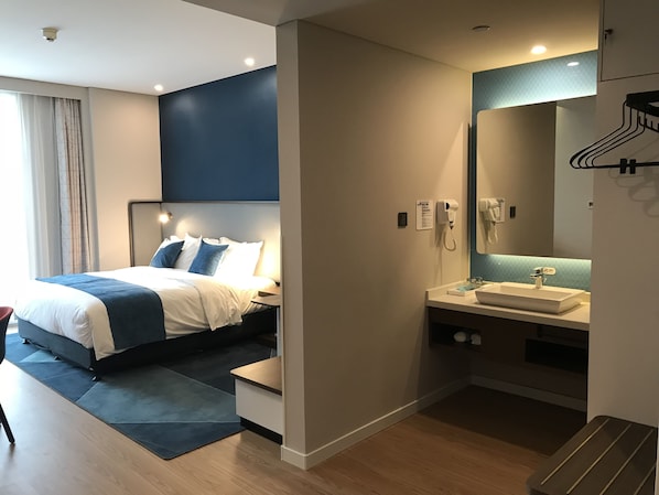A modern hotel room with a bed, bedside table, and a bathroom with a sink and mirror.