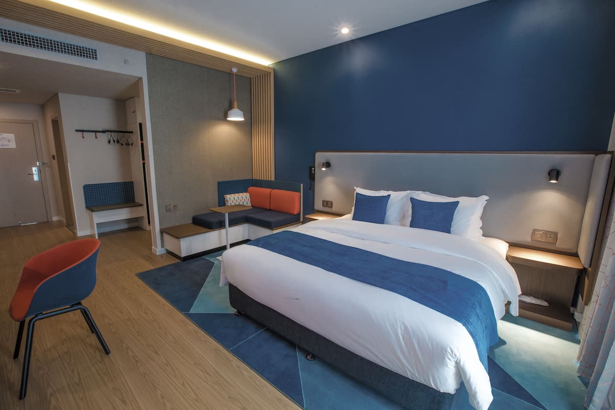 A modern hotel room with a large bed, a seating area with a chair, and a small table.
