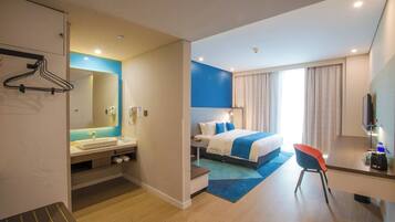 A hotel room with a bed, bedside table, TV, and a bathroom with a sink and mirror.