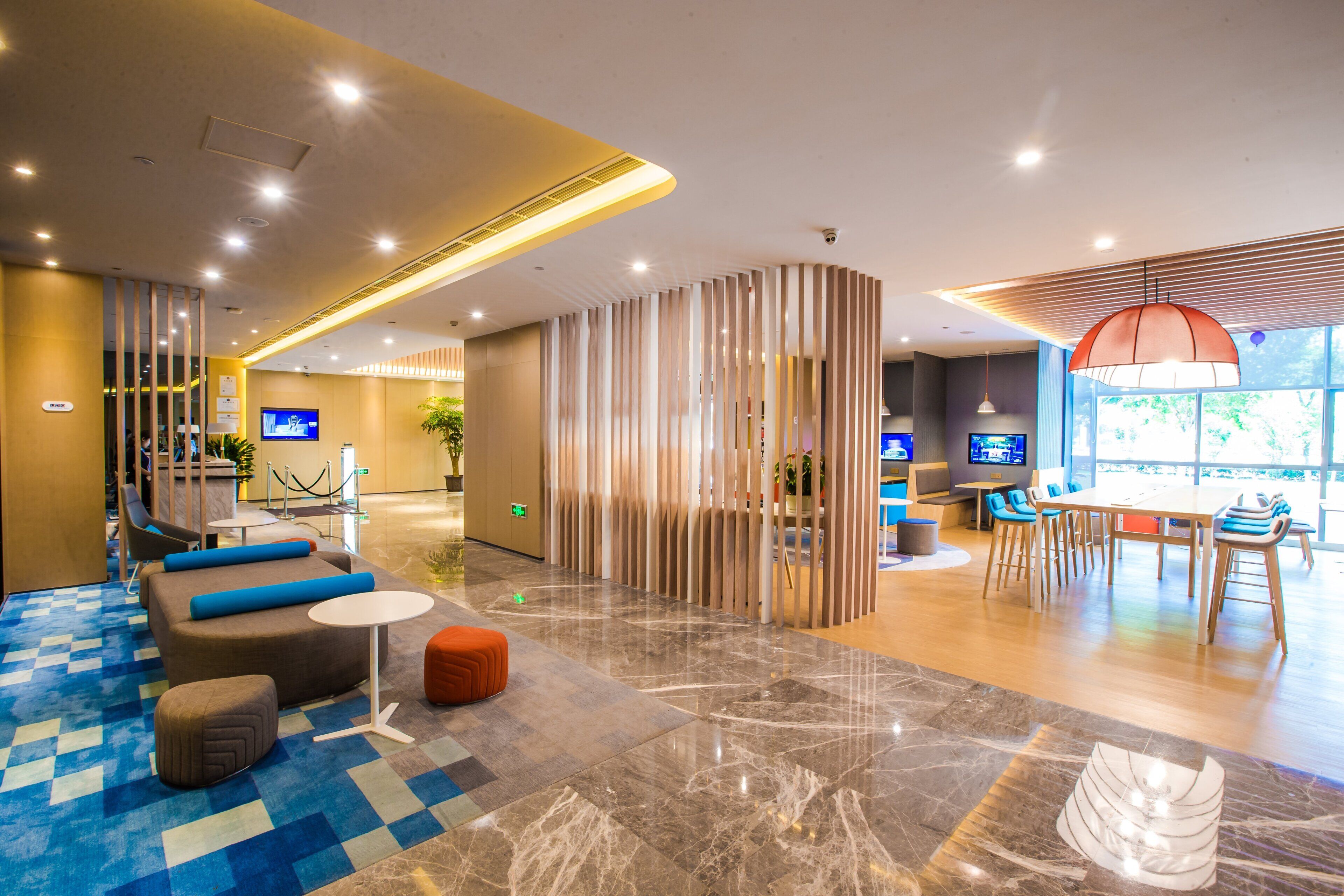 Un hall d’hôtel moderne comprenant un comptoir d’enregistrement, des espaces de détente et un espace repas.