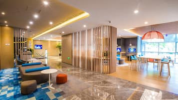 Un hall d’hôtel moderne comprenant un comptoir d’enregistrement, des espaces de détente et un espace repas.