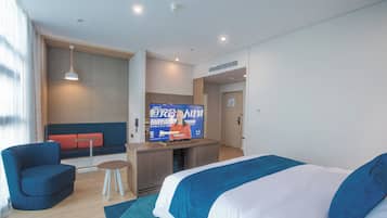 Una camera d'albergo con un letto, una zona salotto con divano e poltrone, un tavolino e una televisione che mostra un canale di notizie.