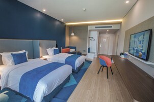 Habitación de hotel con dos camas, un escritorio, una silla y un televisor.