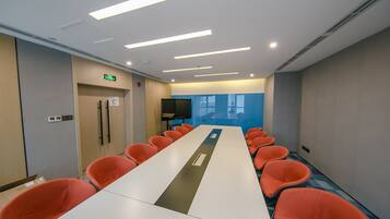 A conference room with a long table, orange chairs, a TV screen, and an exit sign.