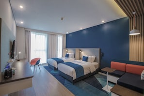A modern hotel room with a large bed, a desk, a chair, and a sofa.