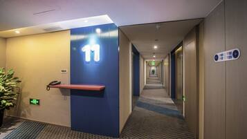 A hotel corridor with a blue wall, a phone on a shelf, and directional signs.